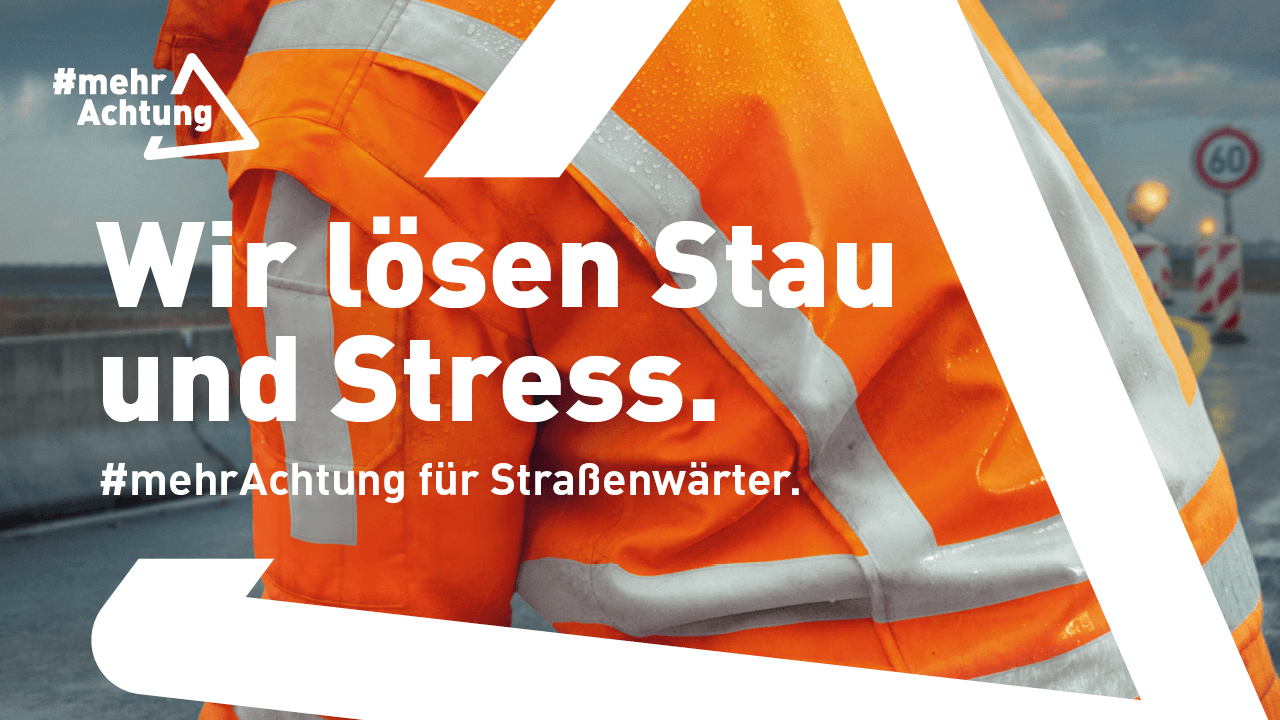 Rückansicht eines Straßenwärters in oranger Warnschutzkleidung bei der Arbeit auf einer nassen Fahrbahn. Im Hintergrund ist eine Baustelle zu erahnen. 