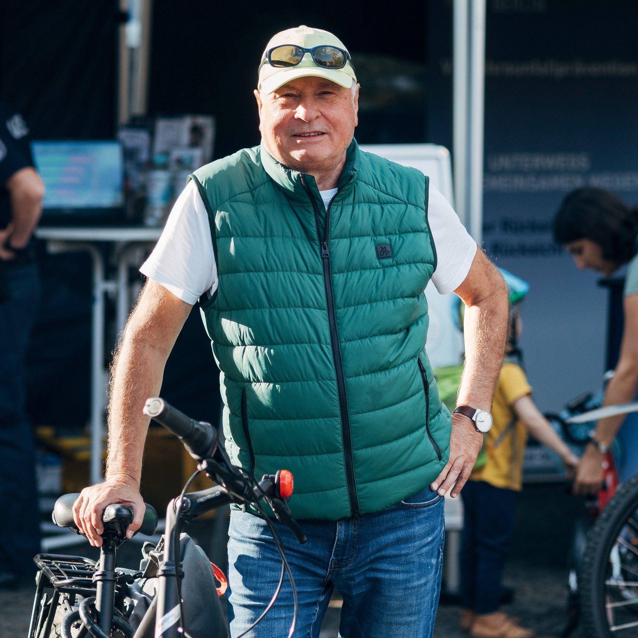 Ein Herr mittleren Alters stützt sich mit der rechten Hand auf sein schwarzes Fahrrad. Im Hintergrund steht ein dunkelblauer Pavillon der Polizei Berlin. 