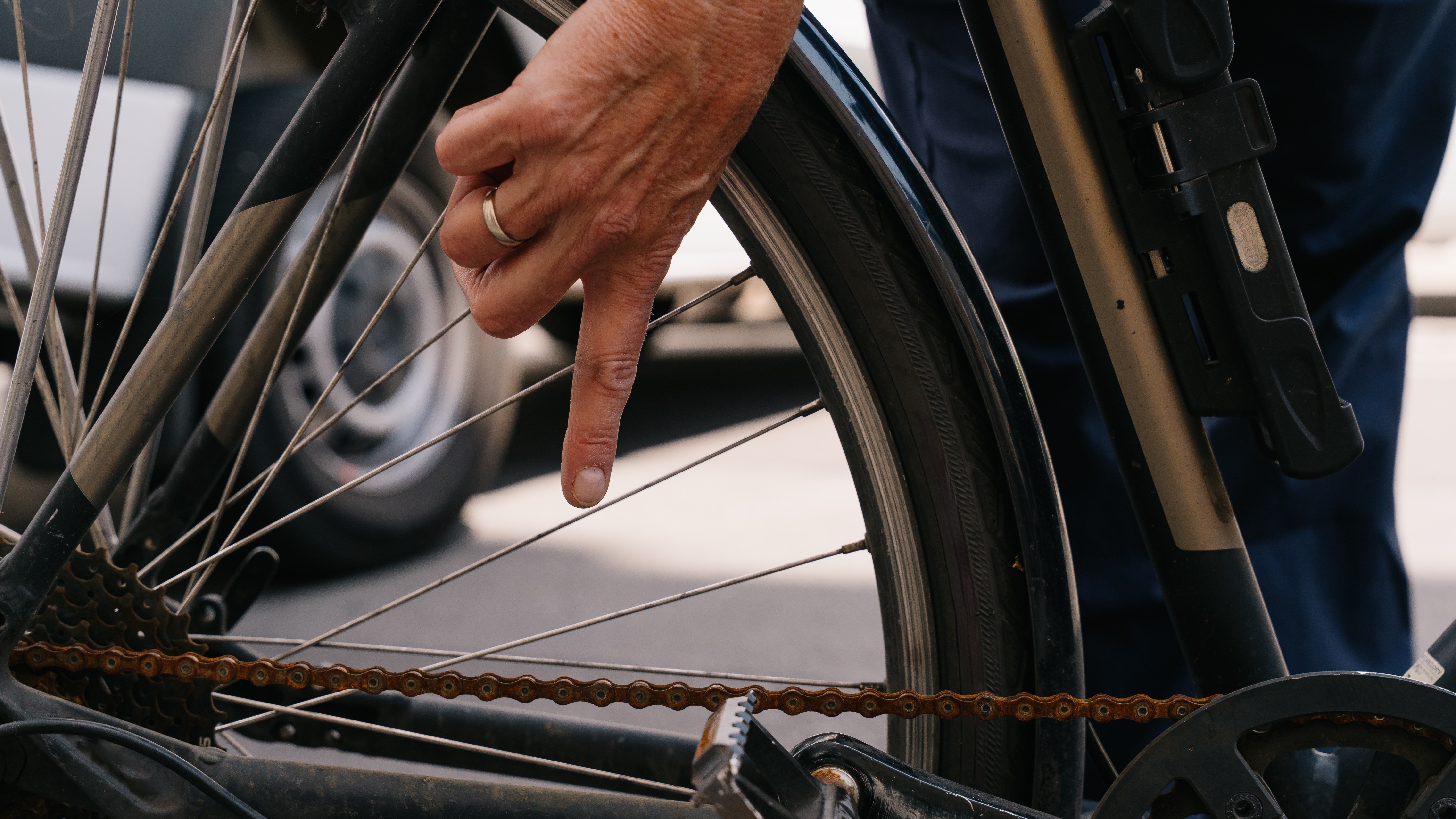 Fahrradcheck Finger an den Speichen 16:9 Nahaufnahme vom Hinterrad eines Fahrrads. Eine Hand zeigt auf die rostige Fahrradkette.