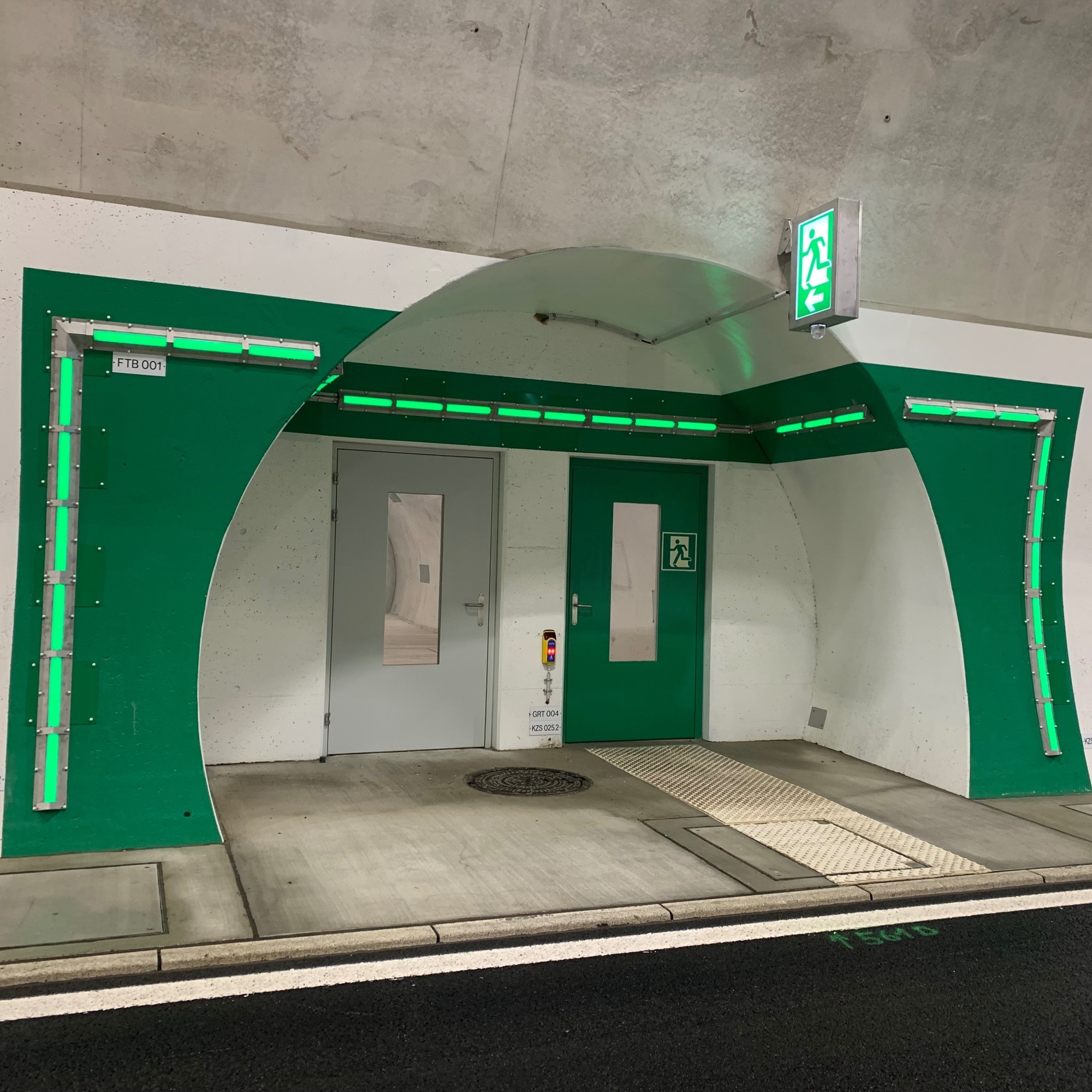 Ein grün umrandeter Notausgang in einer Tunnelröhre. 
